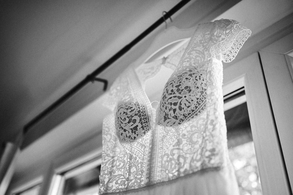 Hochzeitskleid mit dekorativer Spitze hängt an Vorhangstange vor Fenster