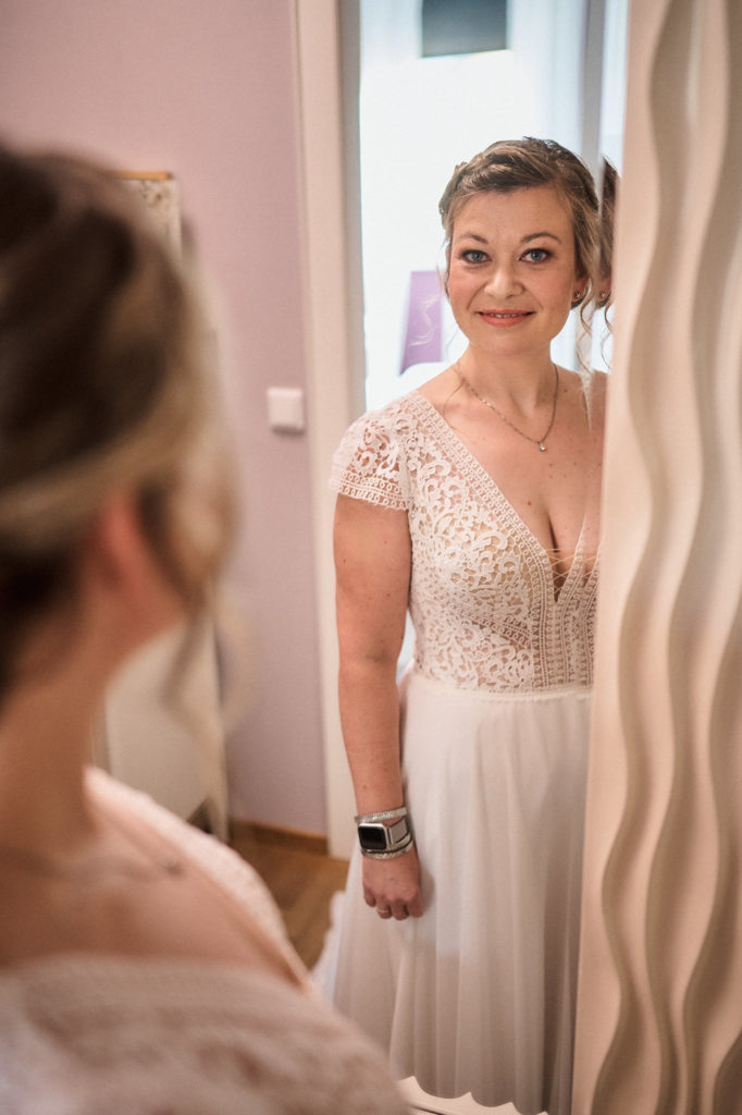 Braut im Kleid fertig gestylt mit Blick in großen Spiegel